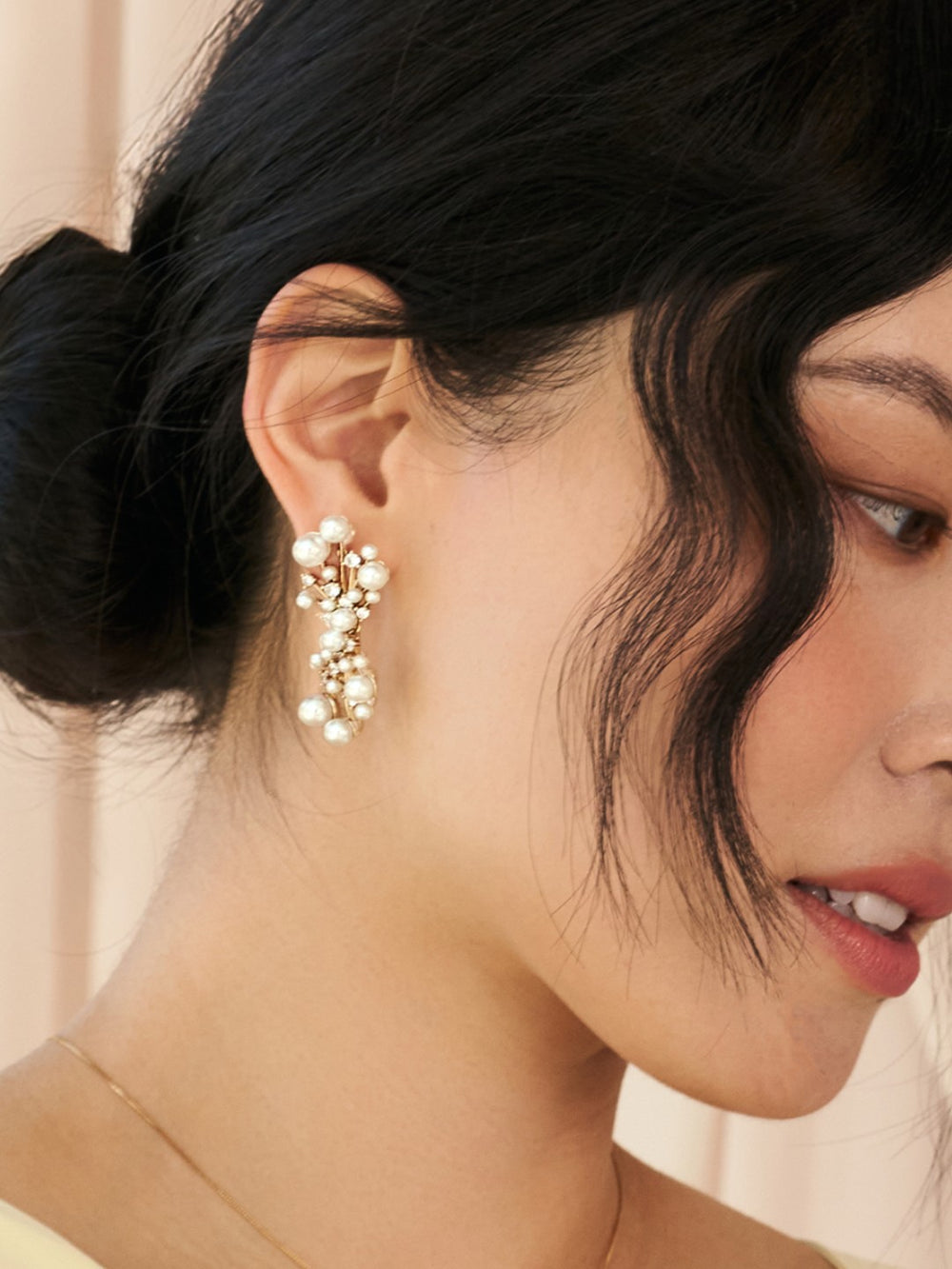 Close-up of a woman wearing a gold earring with pearls against a neutral background