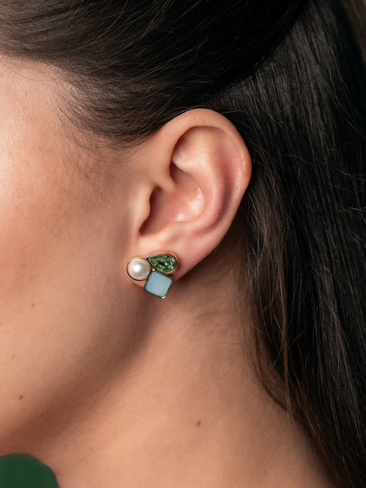 Close-up of an ear wearing a unique earring with green gemstone, pearl, and blue stone.