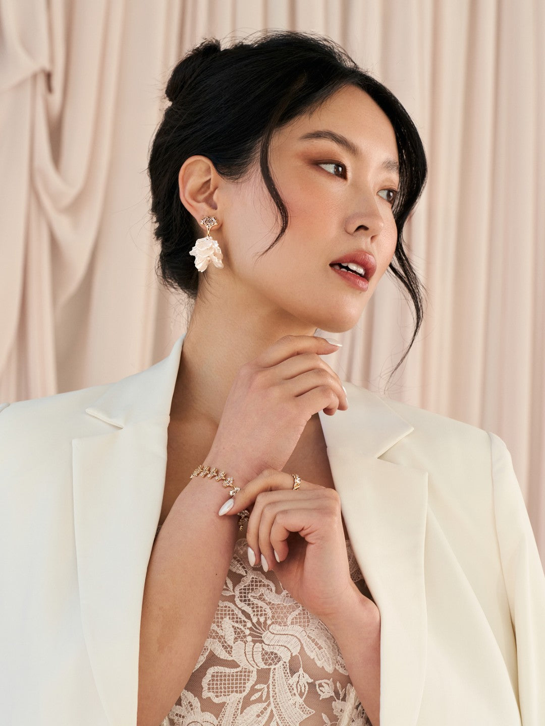 Woman wearing a white blazer over a lace dress with a neutral background