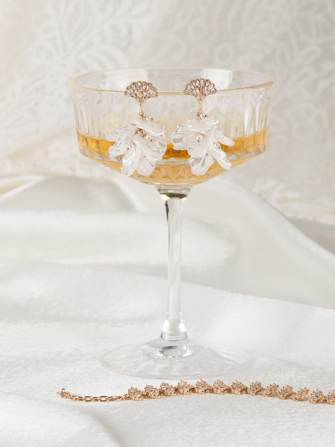 Decorative glass with floral earrings & bracelet on a white surface