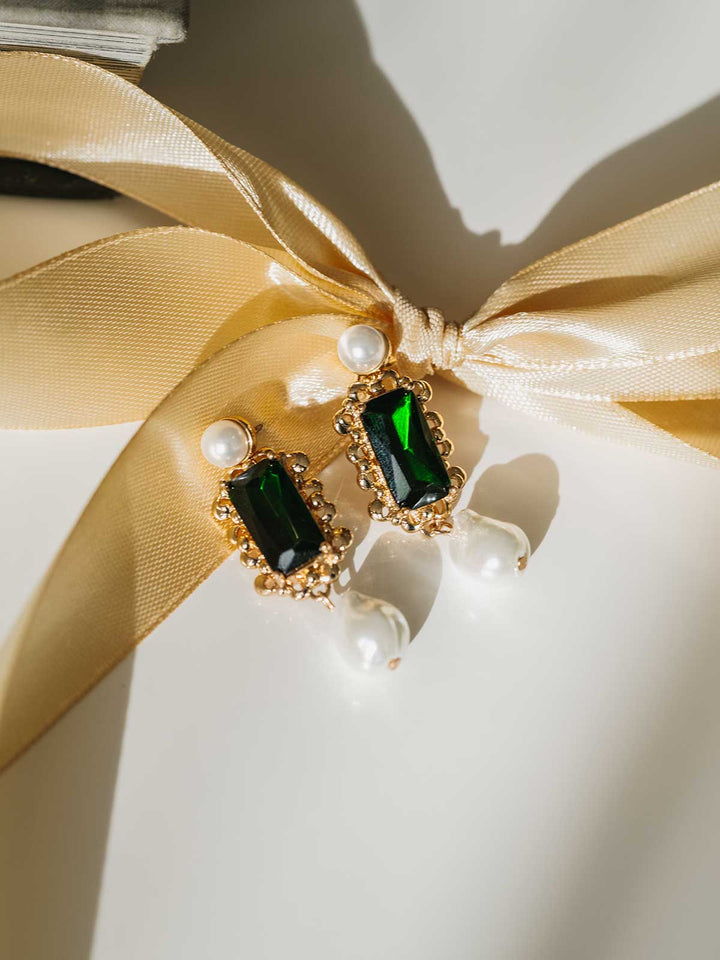 Green gemstone earrings with gold accents on a white background with a gold ribbon.