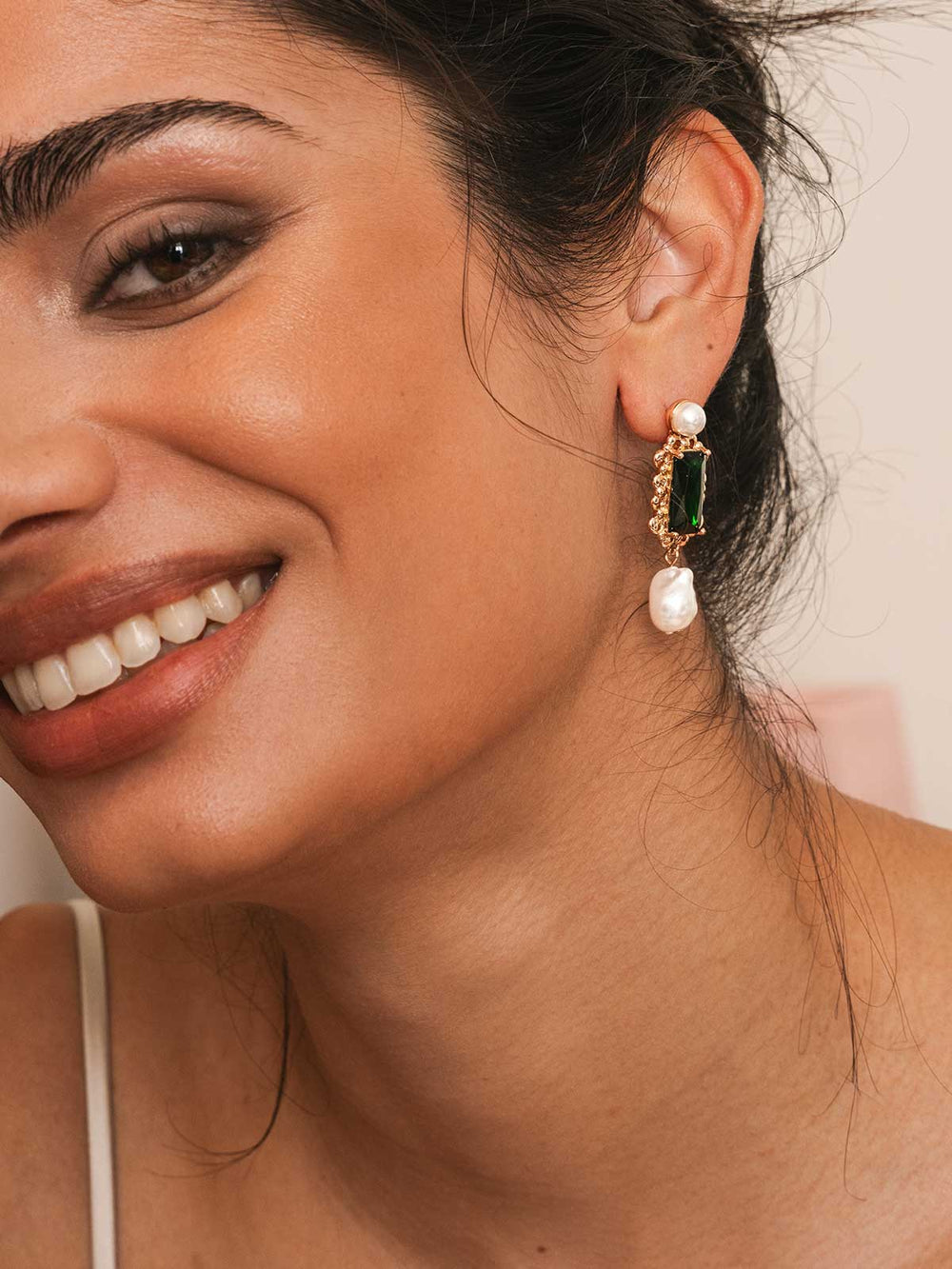 Close-up of a woman wearing elegant earrings with green gemstones and pearls.