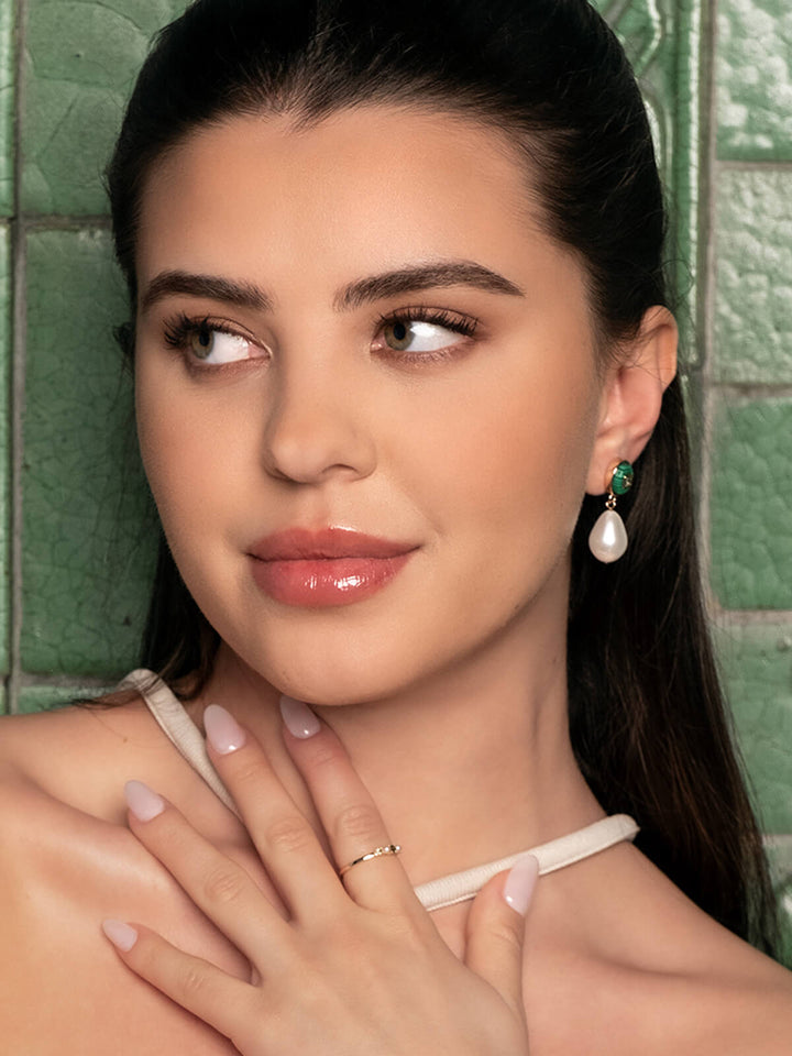 Woman wearing green earrings with a pearl.