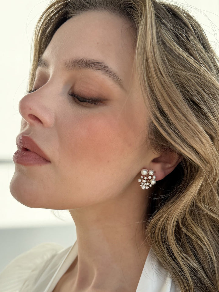 Close-up of a woman wearing pearl stud earrings with a blurred background
