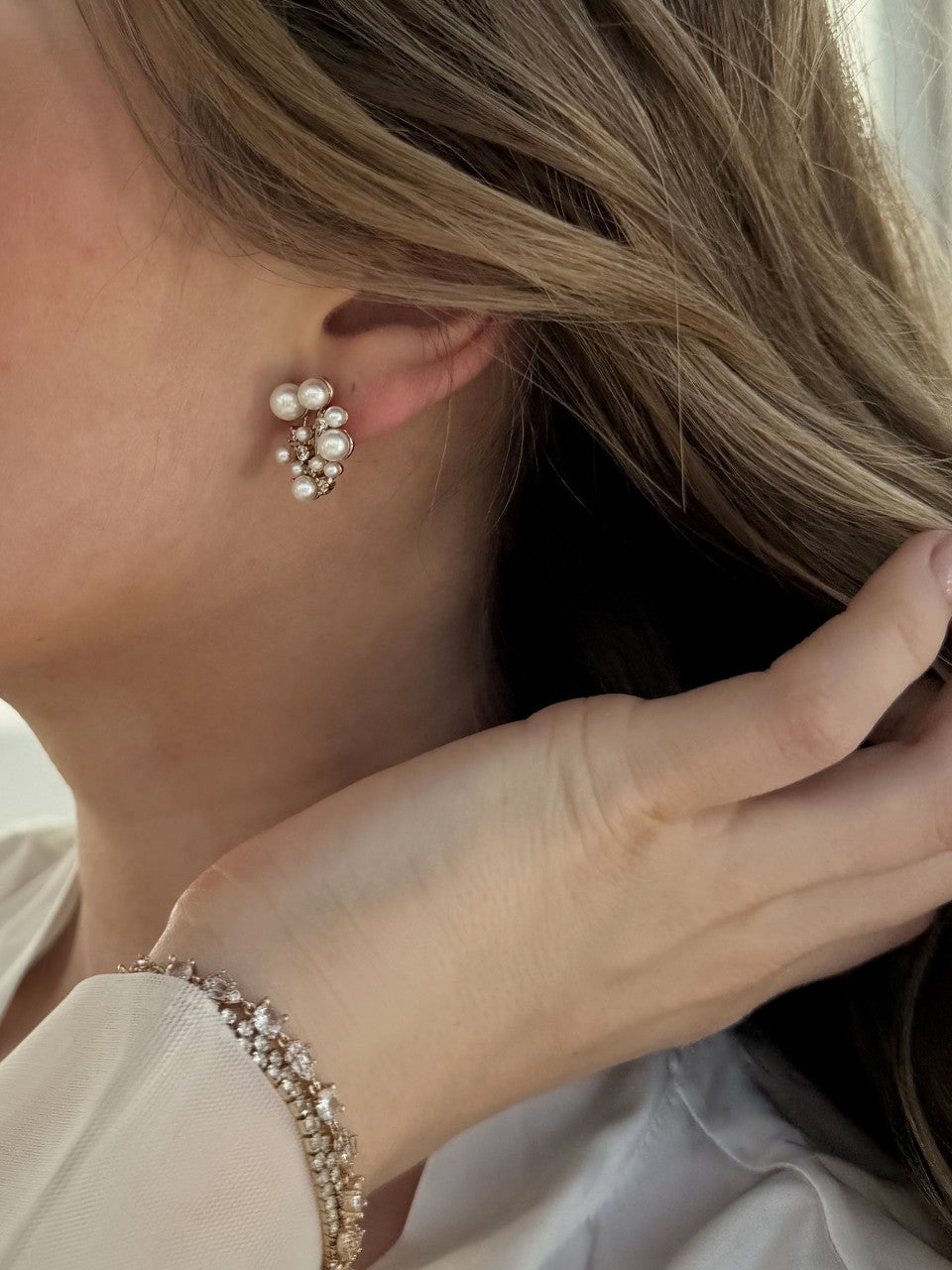 Close-up of a person wearing pearl stud earrings and a matching bracelet.