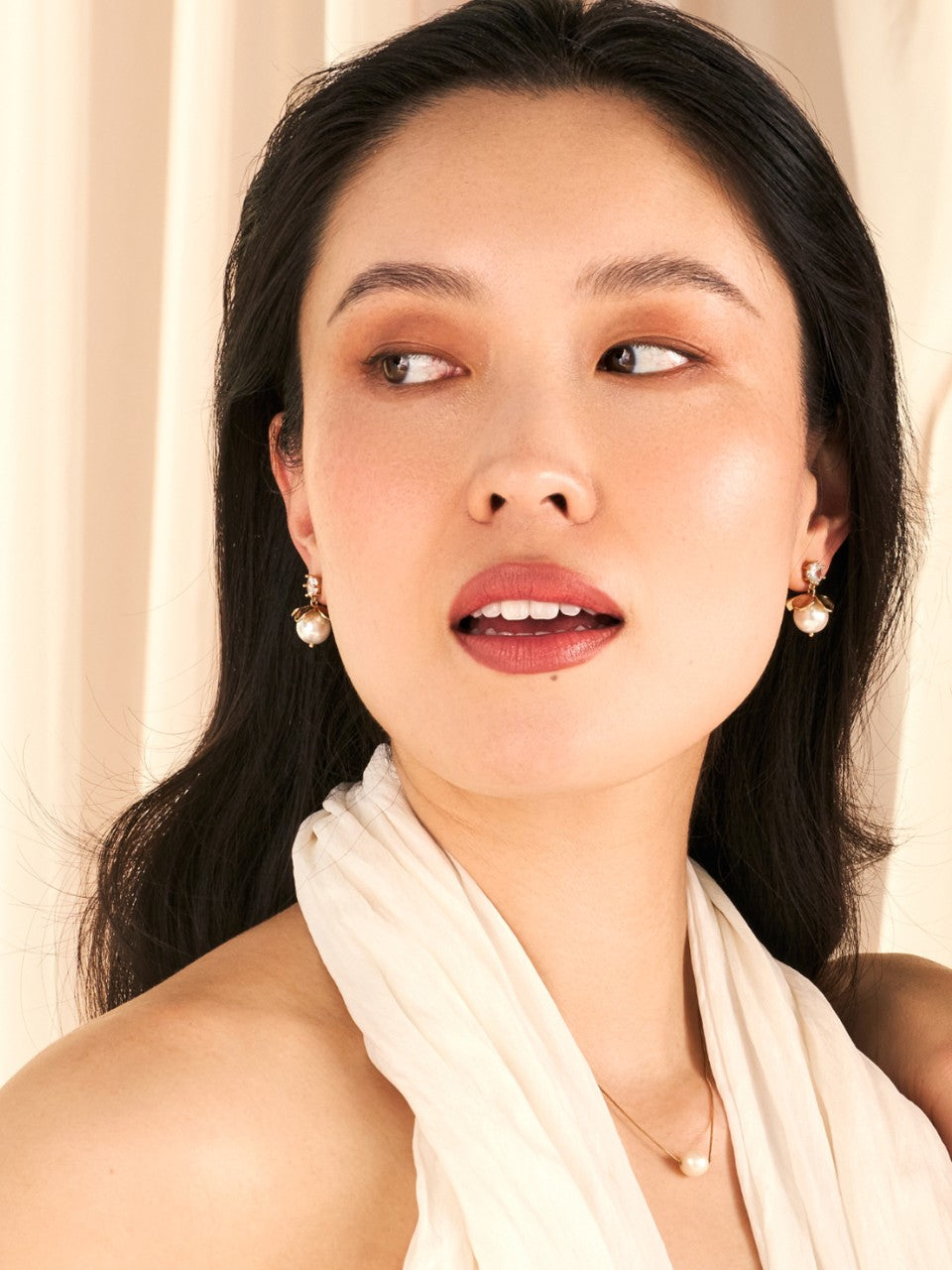 Woman wearing earrings and a light scarf against a neutral background