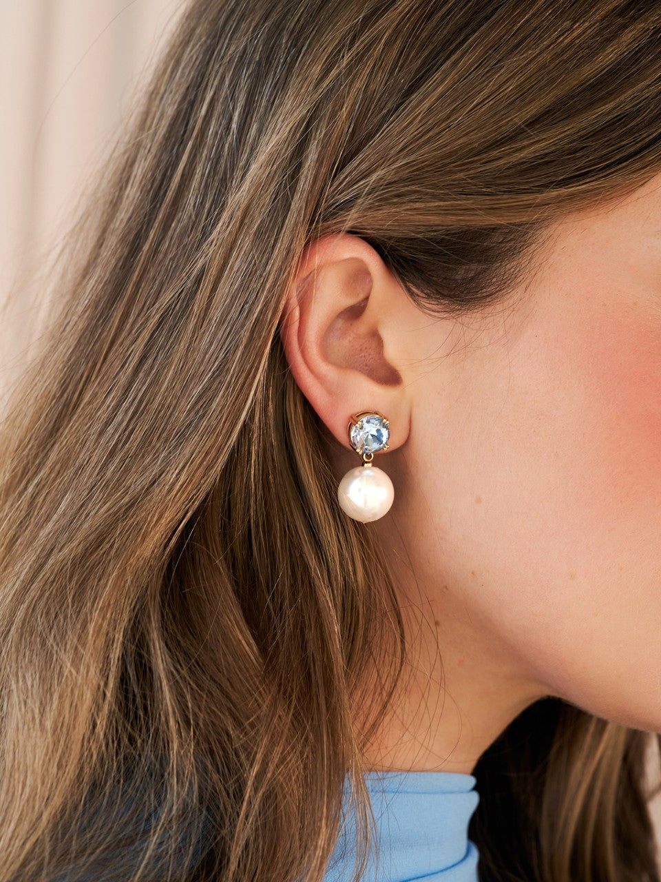 Close-up of an ear wearing a pearl earring with a blue gemstone.