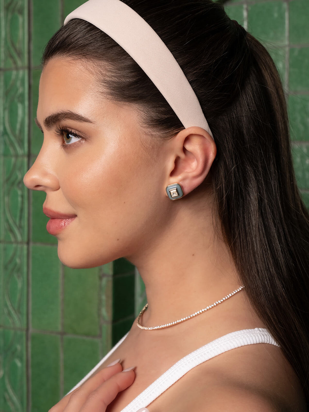 Woman wearing a white headband and earring against a green tiled wall