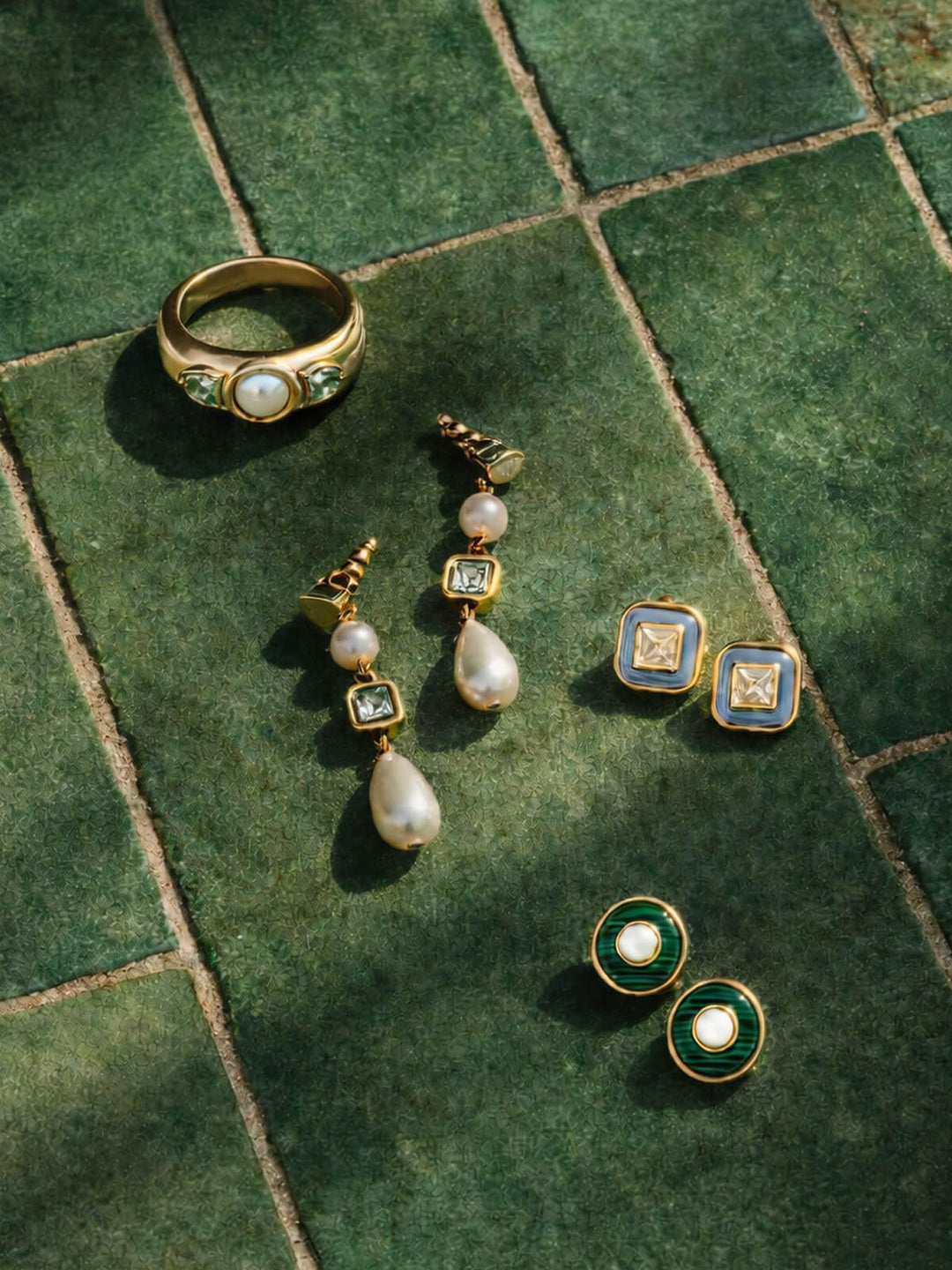 Gold jewelry set with earrings and a ring on a green tiled surface