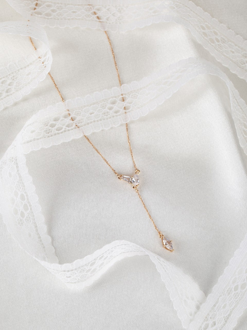 Delicate gold y-necklace on a textured white fabric background