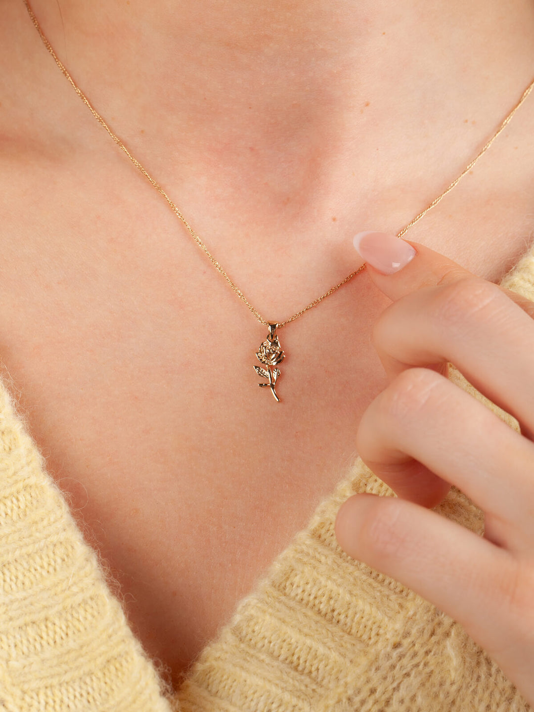 Close-up of a gold rose necklace with a small pendant on a person wearing a yellow sweater.