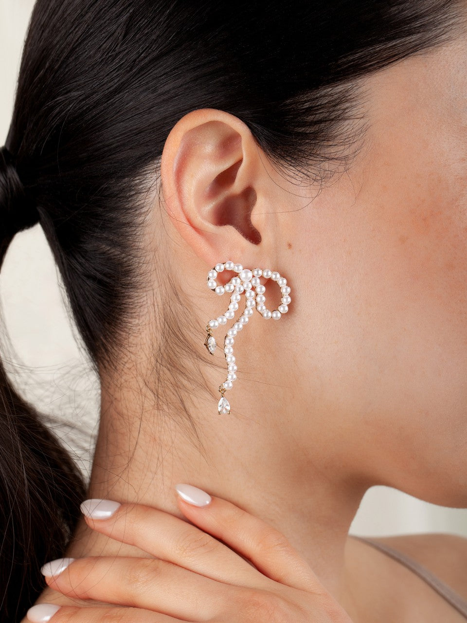 Close-up of a person wearing a delicate pearl bow earrings with a blurred background