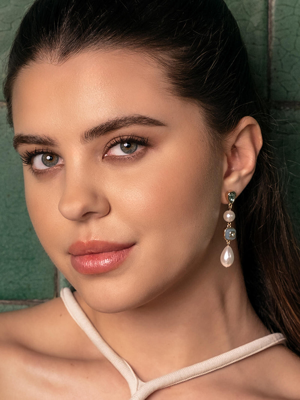 Close-up of a woman wearing pearl earrings with a green background